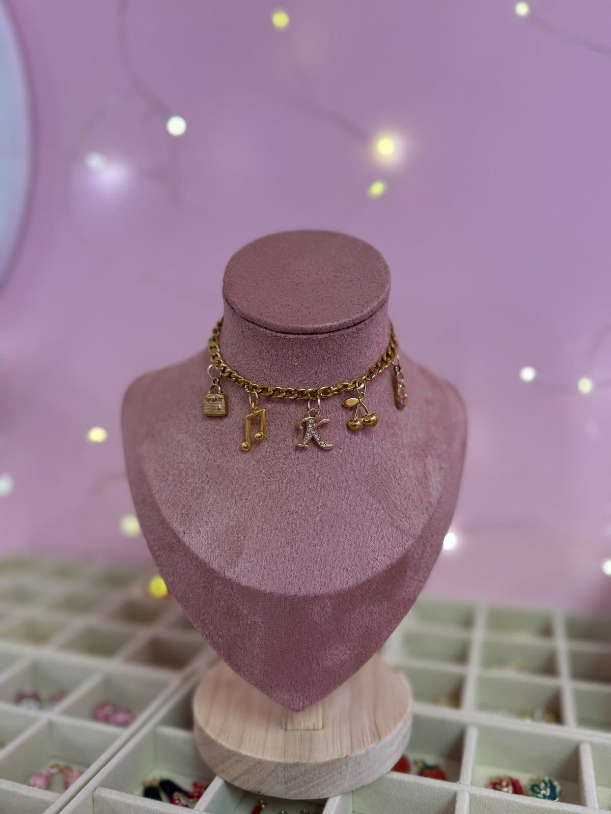 A gold charm necklace with a K initial and music-note charms on a velvet bust